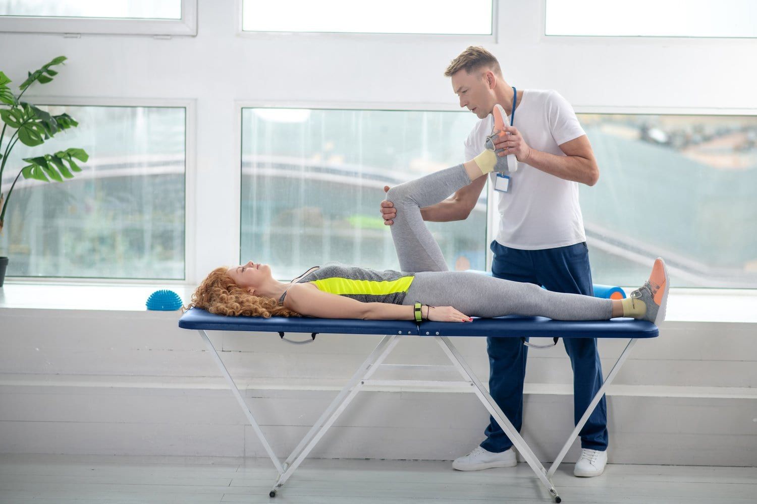 Fizjoterapeuta pracuje z nogą pacjentki leżącej na kozetce w nowoczesnym gabinecie